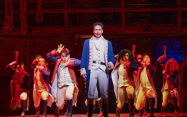 Performers in colonial costumes on stage during a Hamilton musical scene.