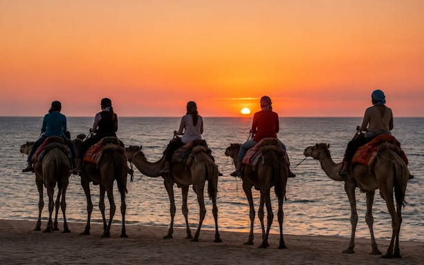 Camel riders at sunset along the Souss River in Agadir.