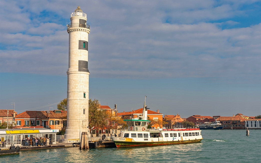 Ferry arriving at Murano, Italy, with colorful buildings and a lighthouse by the canal.