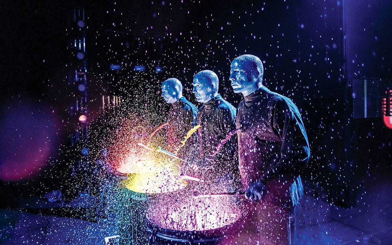 Blue Man Group performing with colorful splashes on stage.