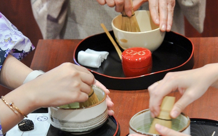 Tourists whisking matcha in bowls during a tea-making class.