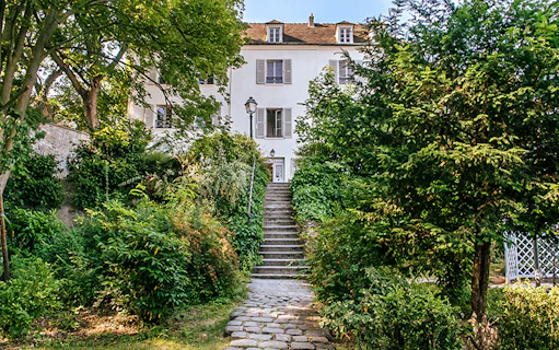 Stone path leading to Montmartre Museum entrance surrounded by lush greenery.