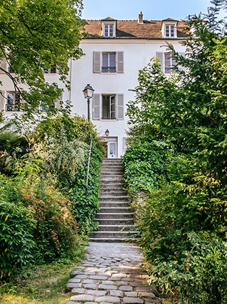 Stone path leading to Montmartre Museum entrance surrounded by lush greenery.