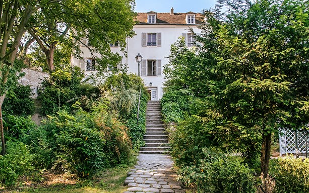 Stone path leading to Montmartre Museum entrance surrounded by lush greenery.