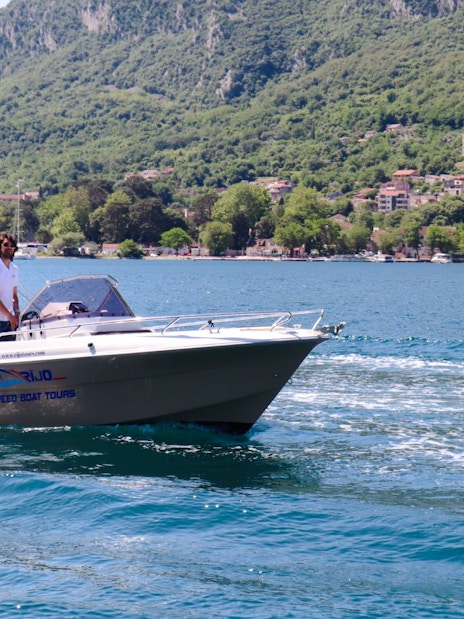 Speedboat on water with Perast town and green hills in the background.