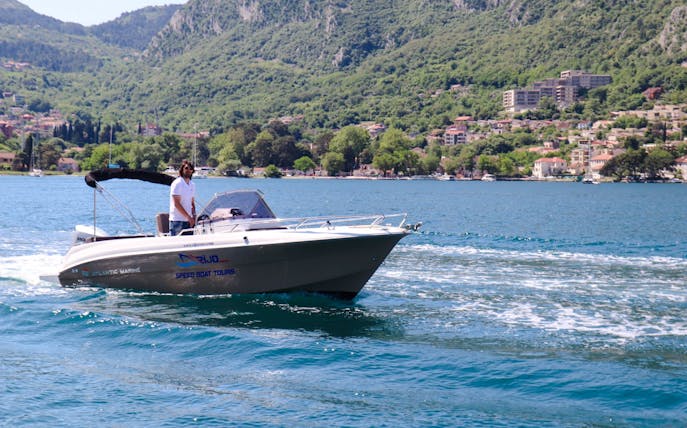 Speedboat on water with Perast town and green hills in the background.