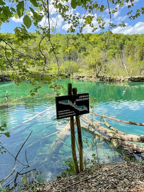 Plitvice Lakes National Park turquoise lake view with wooden sign and lush greenery.