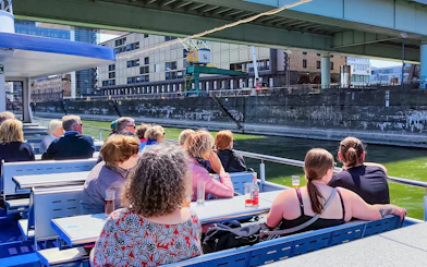 Cruise passengers on deck viewing Cologne harbor buildings.