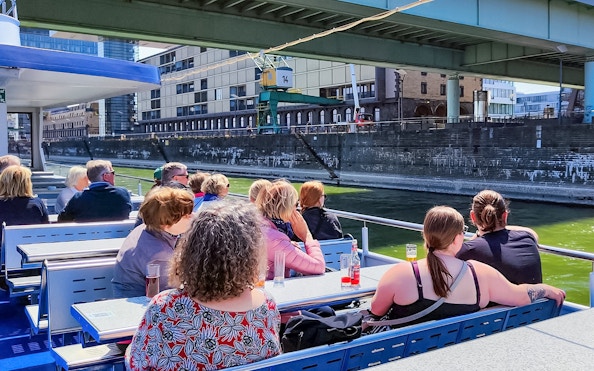 Cruise passengers on deck viewing Cologne harbor buildings.