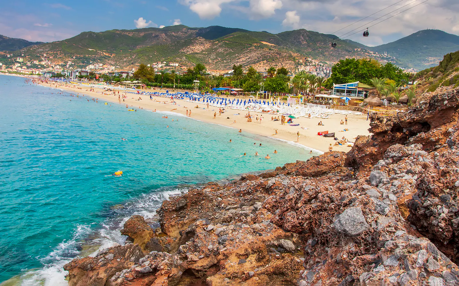 Alanya beach with cable cars and mountains in the background.