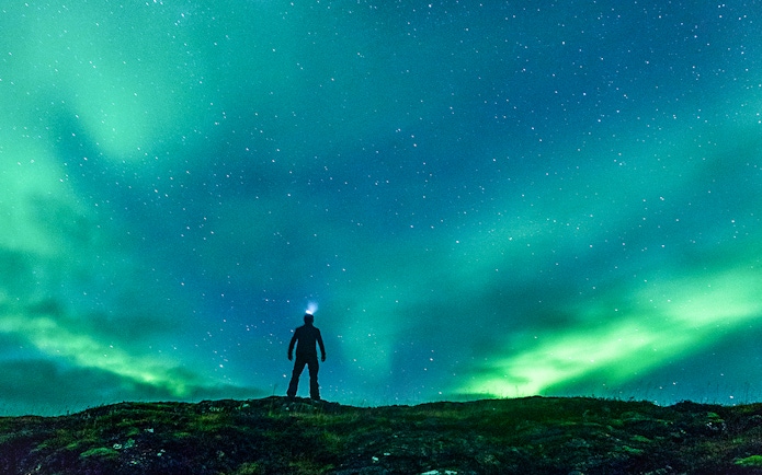 Silhouette of a person under the Northern Lights on an off-road tour.