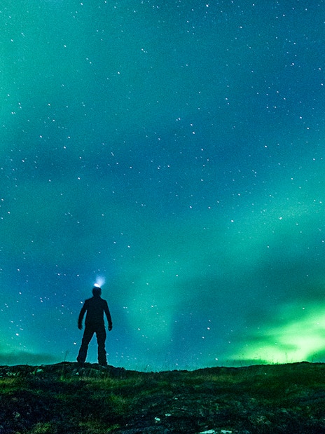 Silhouette of a person under the Northern Lights on an off-road tour.