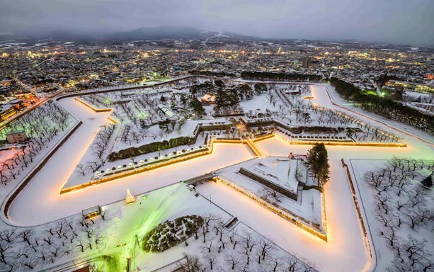 Aerial view of snow-covered Goryokaku Fort in Hakodate, Japan, with illuminated star-shaped moat.