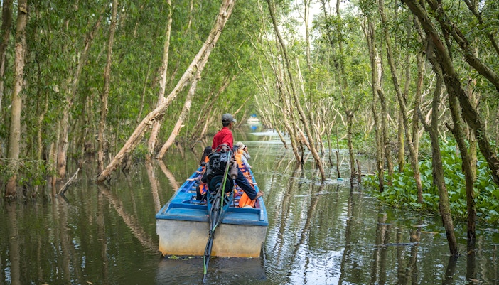 People on motorboat exploring Mekong Delta, Vietnam, surrounded by lush greenery and calm waters.