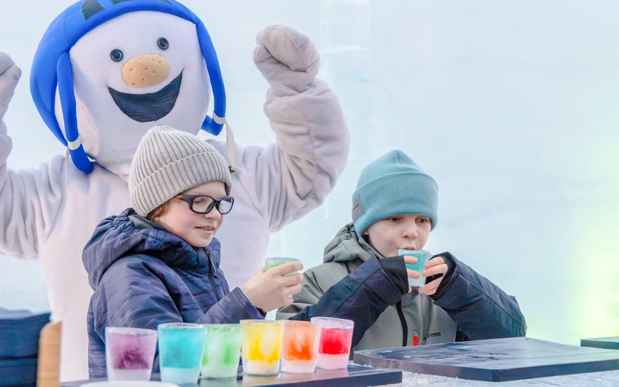 Children enjoying colorful drinks with a snowman character at Snowman World, Santa Claus Village.