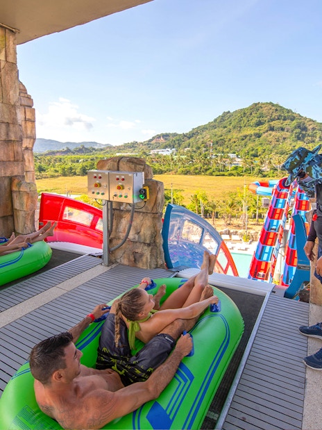 Visitors on inflatable rafts at Andamanda Phuket water slide with scenic mountain view.