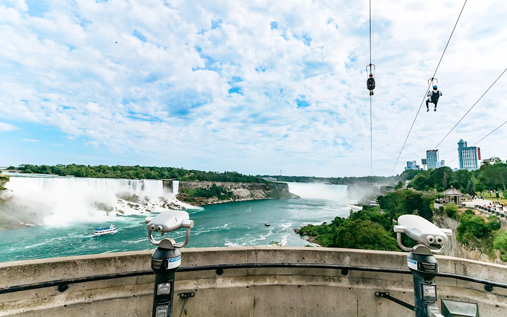 Ziplining over Niagara Falls with city skyline and waterfalls in view.