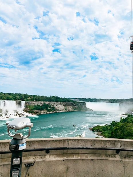 Ziplining over Niagara Falls with city skyline and waterfalls in view.
