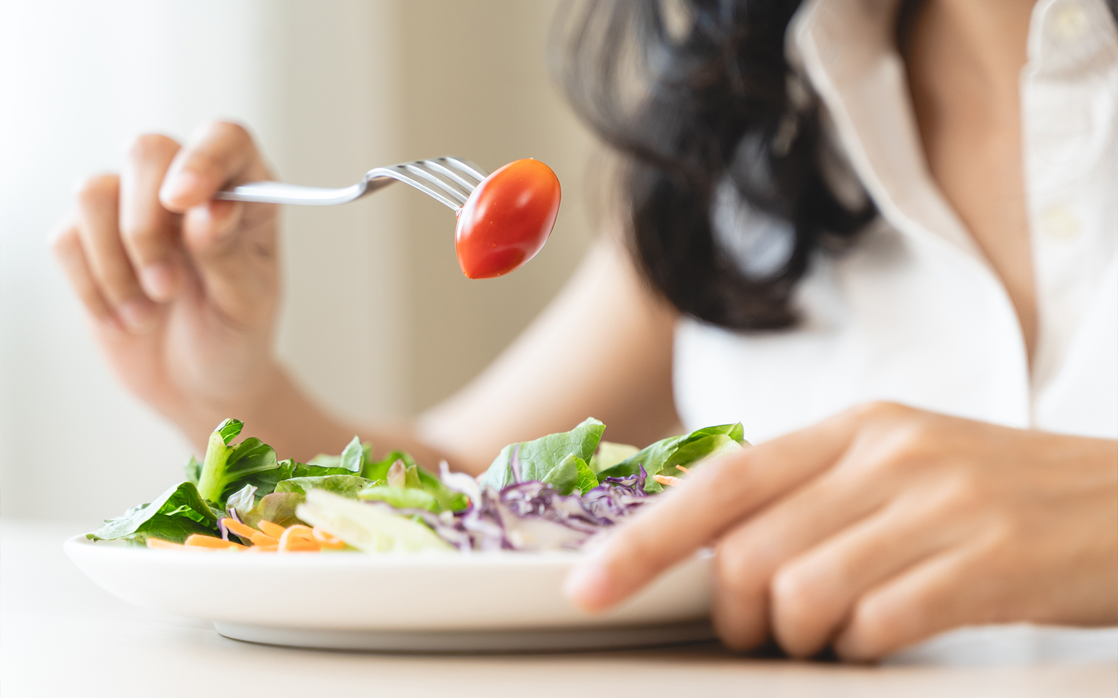 Person eating a garden salad with cherry tomato on fork.