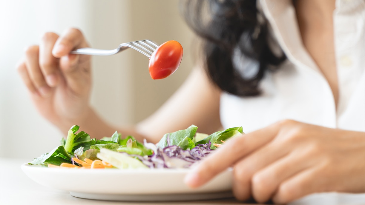 Person eating a garden salad with cherry tomato on fork.
