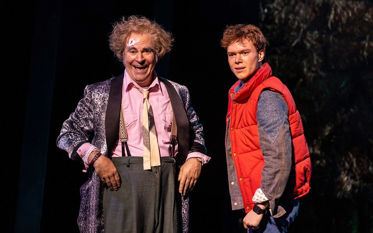 Two actors on stage in a "Back to the Future" performance, one in a red vest.