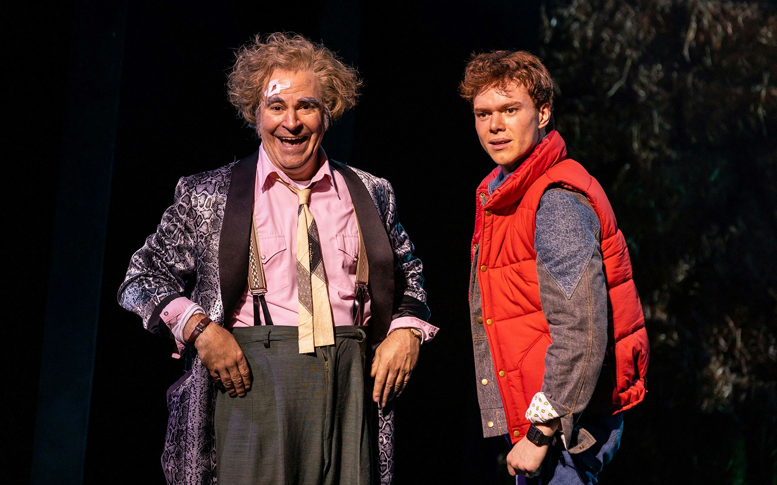 Two actors on stage in a "Back to the Future" performance, one in a red vest.