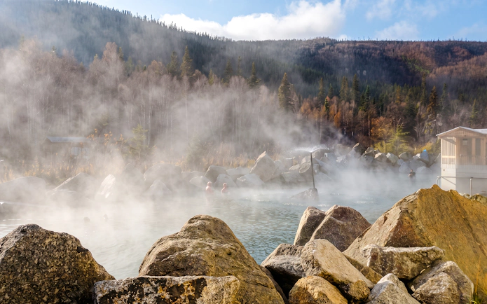 Steaming Chena Hot Springs surrounded by rocky landscape and forested hills.