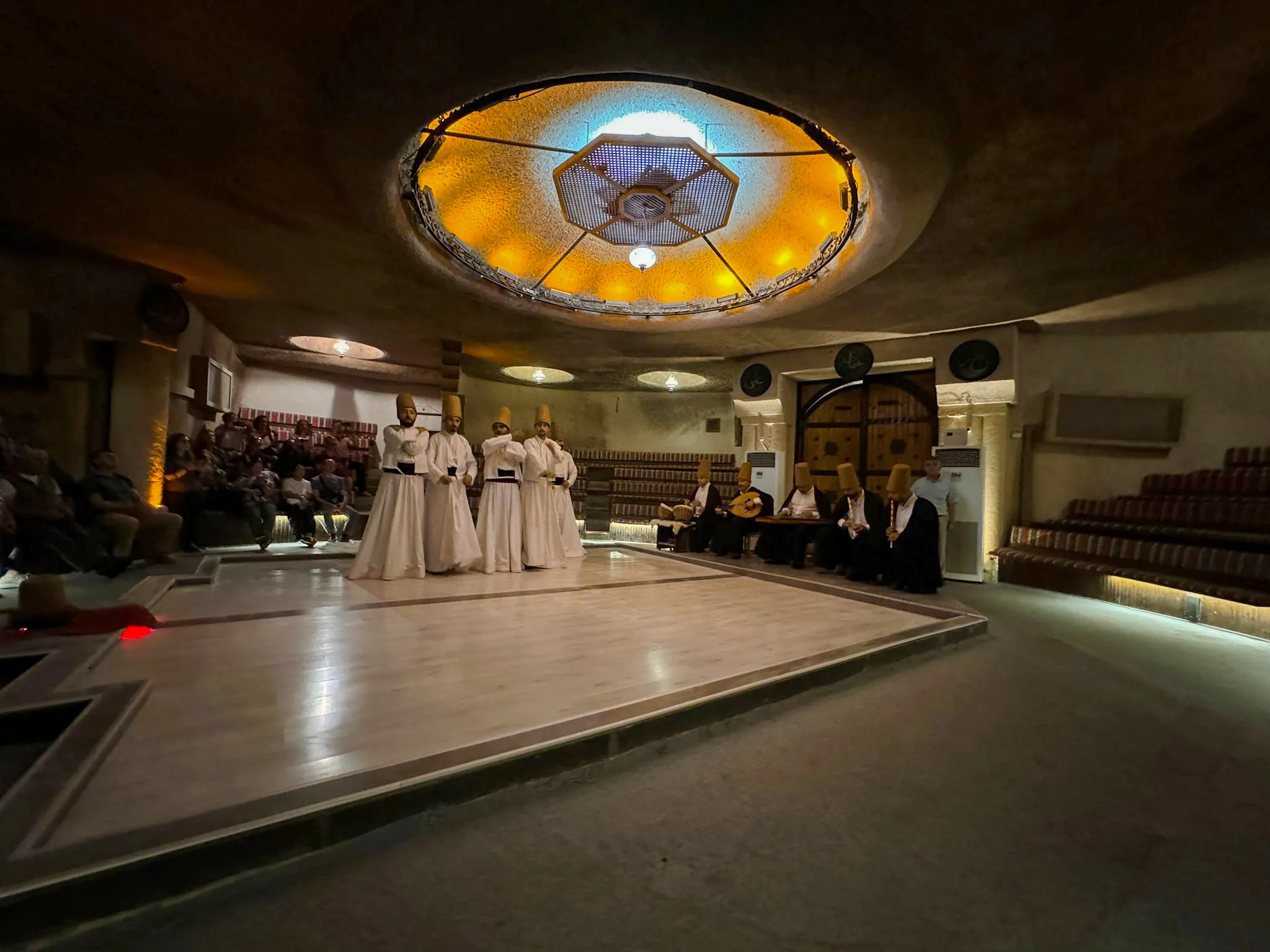 Whirling dervishes performing in a Cappadocia ceremony hall with musicians.