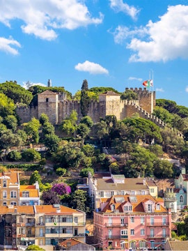 Castelo de S. Jorge in Lisbon with surrounding colorful buildings and lush greenery.