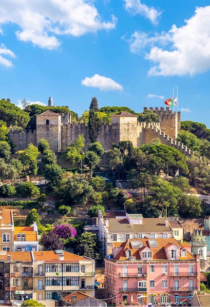 Castelo de S. Jorge in Lisbon with surrounding colorful buildings and lush greenery.