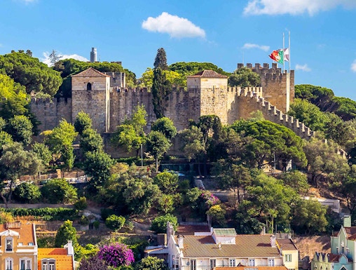 Castelo de S. Jorge in Lisbon with surrounding colorful buildings and lush greenery.