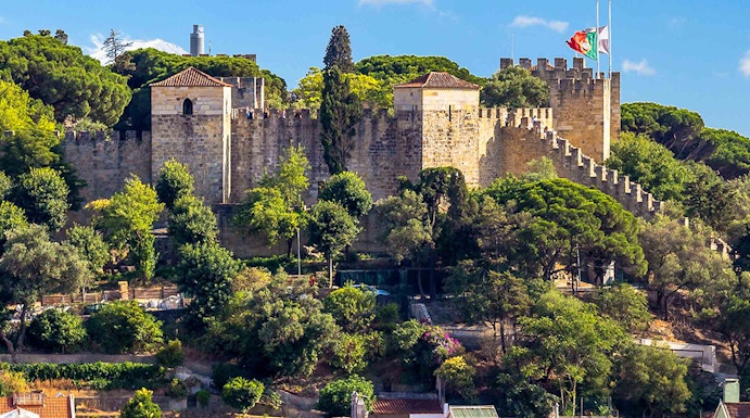Castelo de S. Jorge in Lisbon with surrounding colorful buildings and lush greenery.