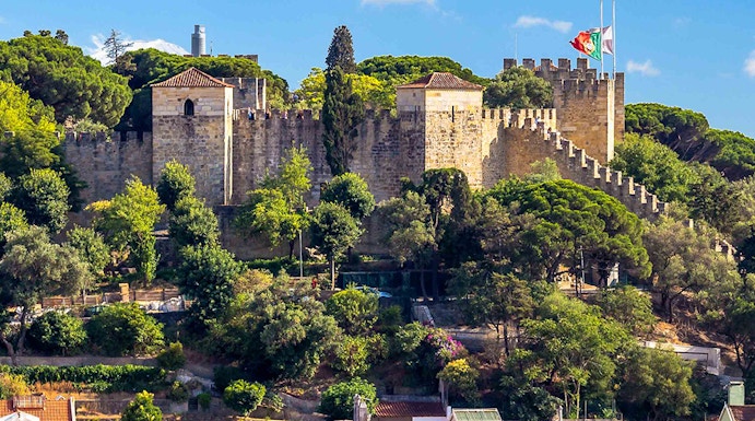 Castelo de S. Jorge in Lisbon with surrounding colorful buildings and lush greenery.