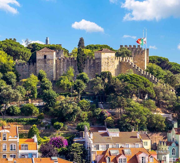Castelo de S. Jorge in Lisbon with surrounding colorful buildings and lush greenery.
