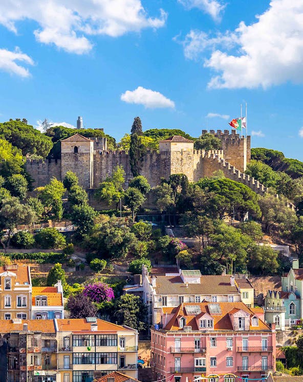 Castelo de S. Jorge in Lisbon with surrounding colorful buildings and lush greenery.
