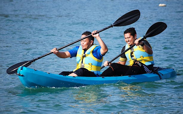 Two people kayaking at Paradise 101, wearing life jackets and paddling on clear water.