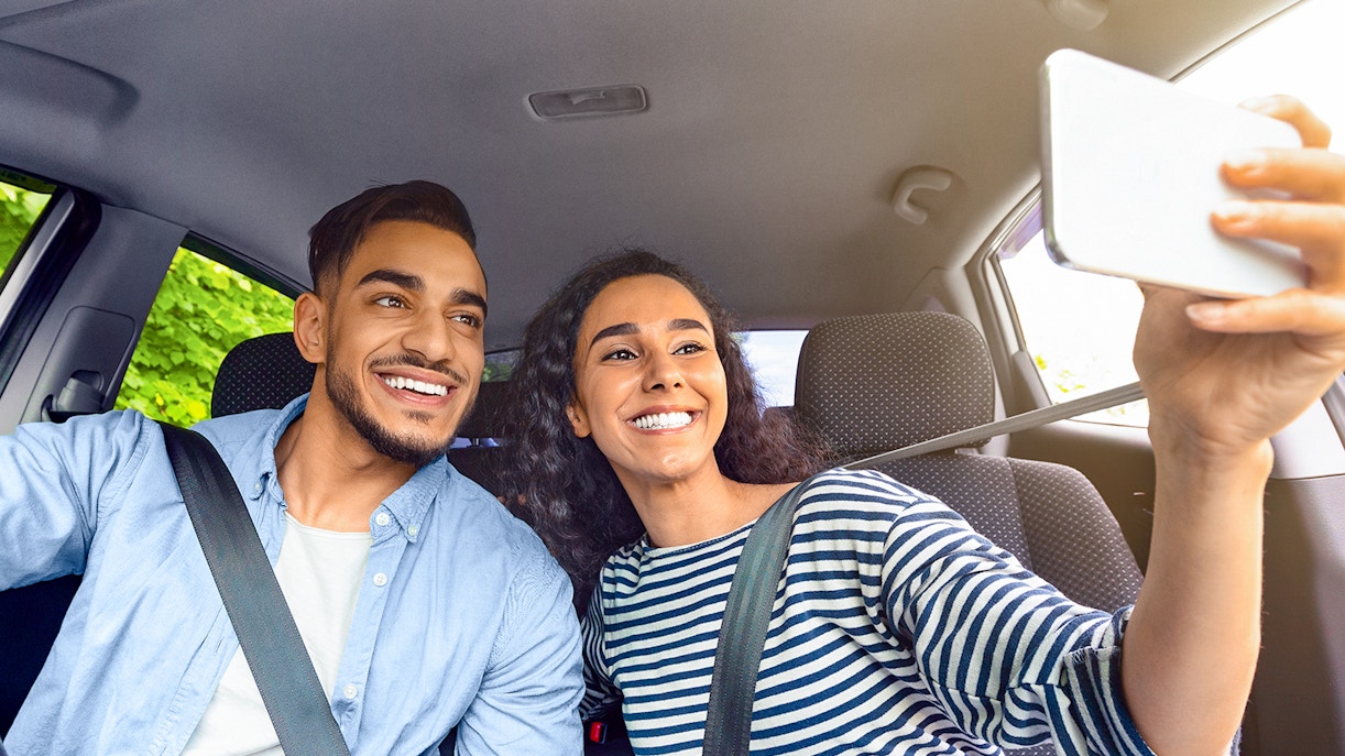 Couple taking selfie in car, wearing summer clothes.