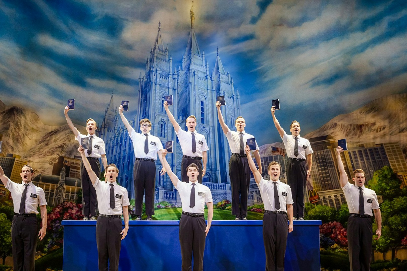Cast performing The Book of Mormon on stage in Brisbane, with a backdrop of a temple.