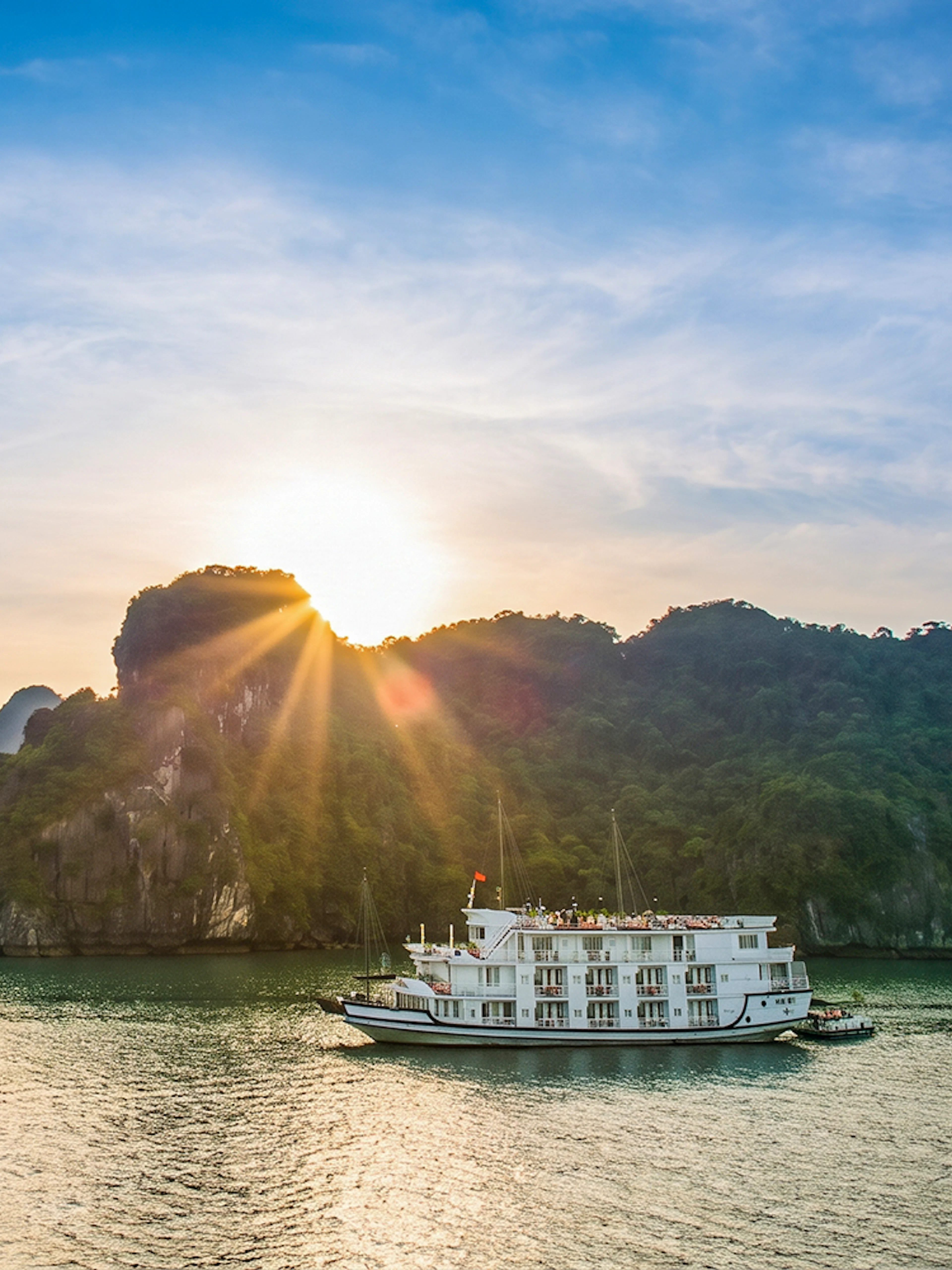 Cruise ship sailing in Halong Bay at sunset with limestone islands in the background.