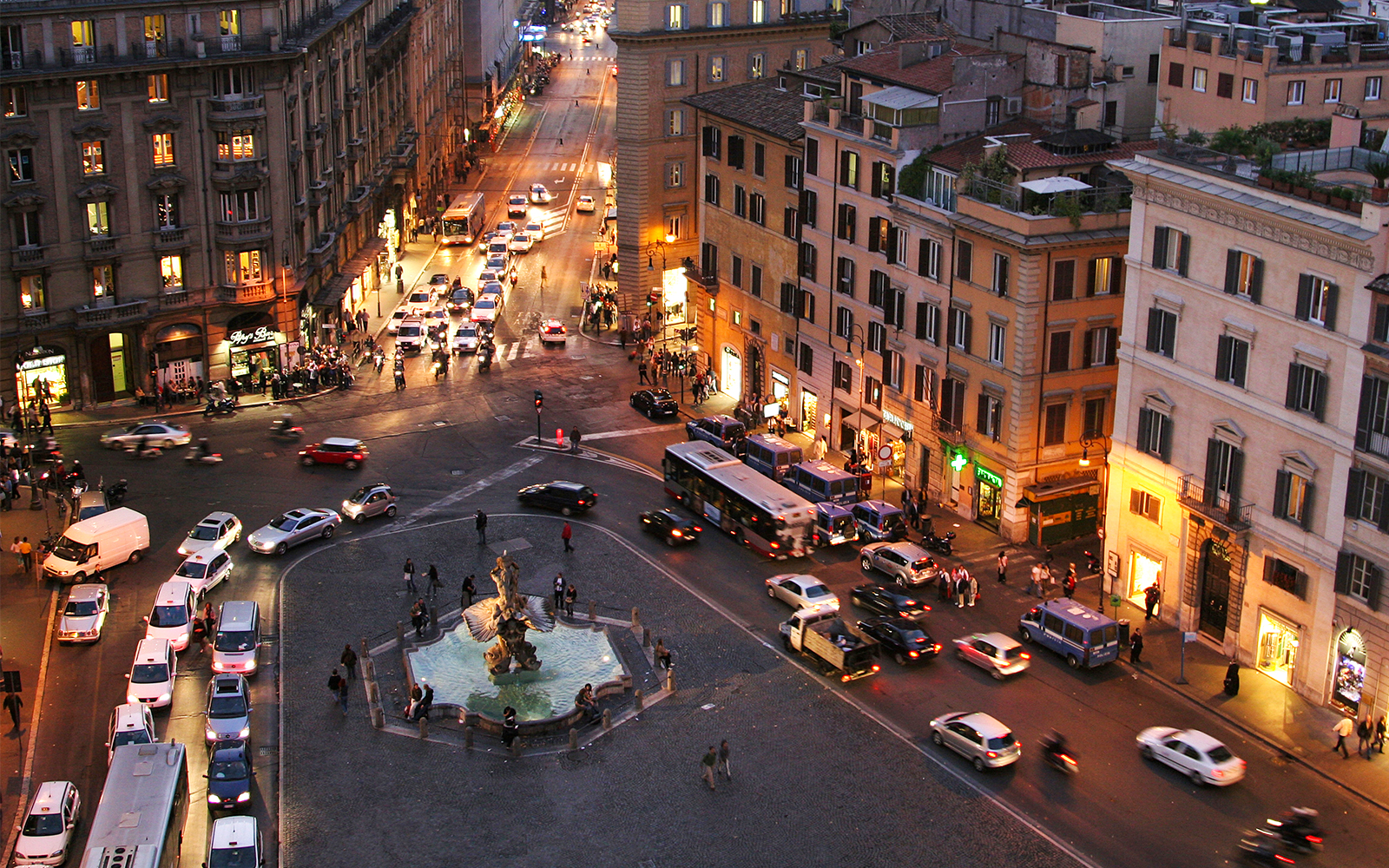 Rome cityscape at night with busy streets and illuminated buildings, featuring a central fountain.