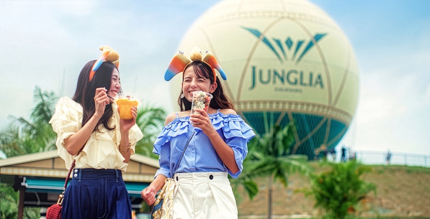 Visitors enjoying snacks at Junglia Okinawa theme park with iconic balloon in background.