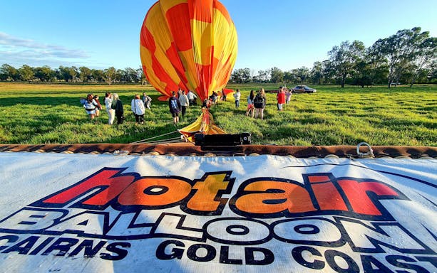Hot air balloon preparation in a grassy field, Cairns, with a group of people nearby.