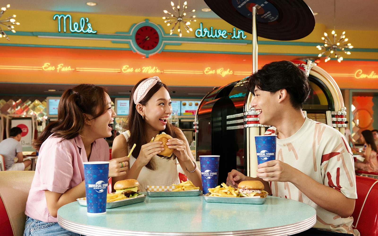 Three friends enjoying burgers and fries at Mel's Dine-In, Universal Studios Singapore.