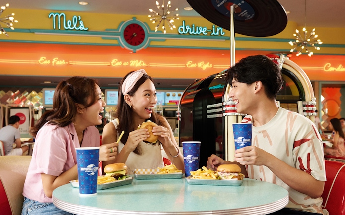 Three friends enjoying burgers and fries at Mel's Dine-In, Universal Studios Singapore.