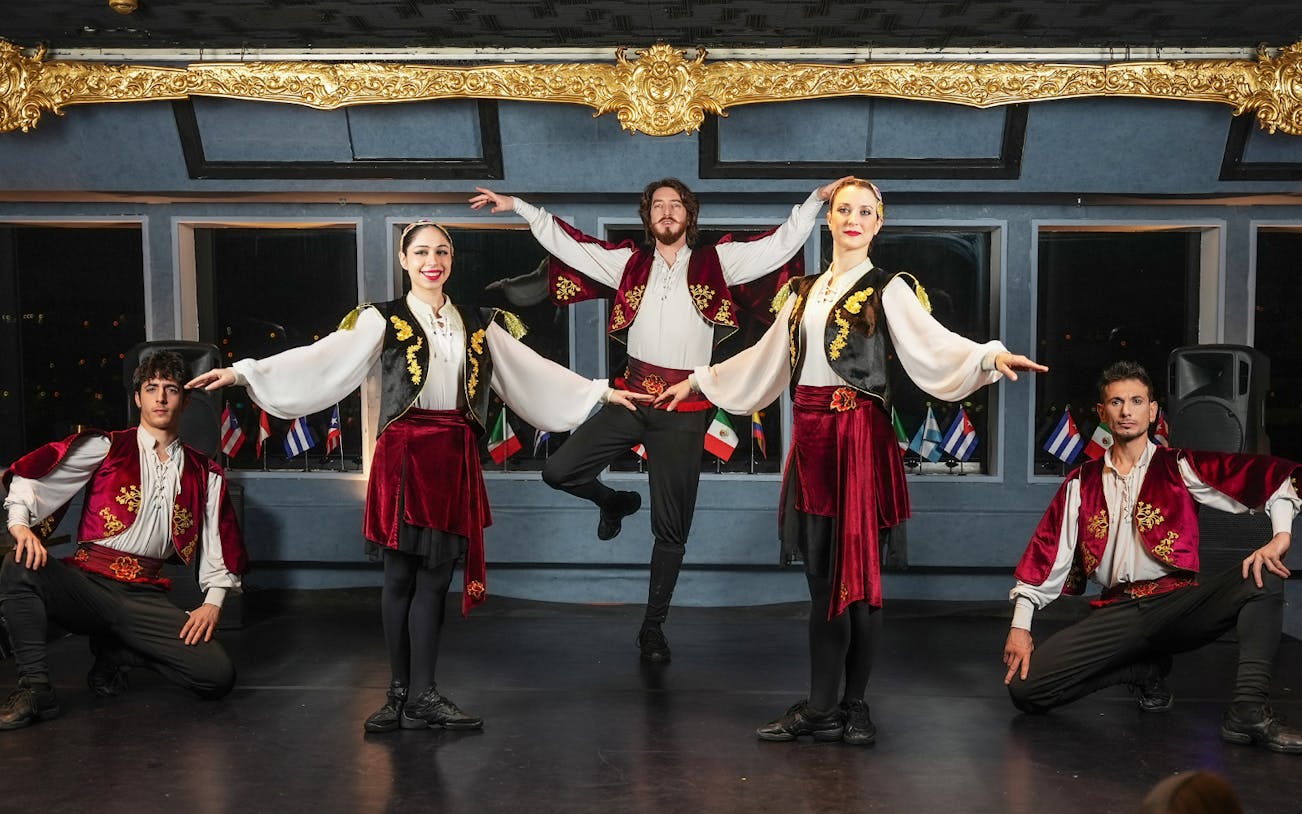 Traditional dancers performing on a Bosphorus dinner cruise with flags in the background.