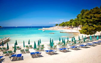Sun loungers and umbrellas on Ksamil beach, Albania, with turquoise water and trees in the background.