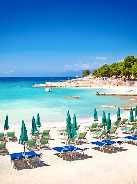 Sun loungers and umbrellas on Ksamil beach, Albania, with turquoise water and trees in the background.