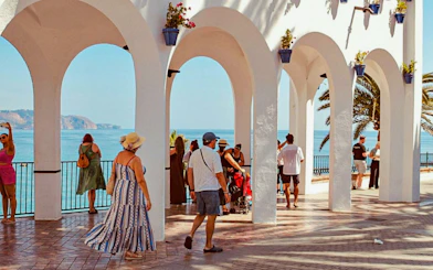 Tourists enjoying the view from Balcon de Europa in Nerja, Spain, with ocean and arches.
