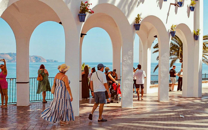 Tourists enjoying the view from Balcon de Europa in Nerja, Spain, with ocean and arches.