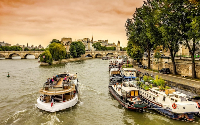 Seine River cruise boat passing under Paris bridge with cityscape in background.